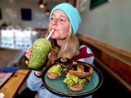 woman drinking green smoothie whilst holding breakfast